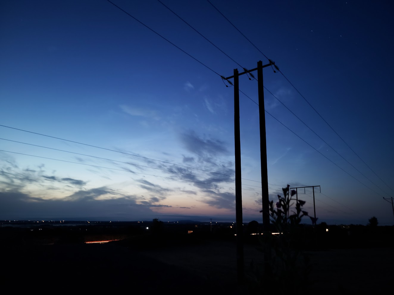 Telecommunications towers and power lines silhouetted against a deep blue evening sky in Galway.