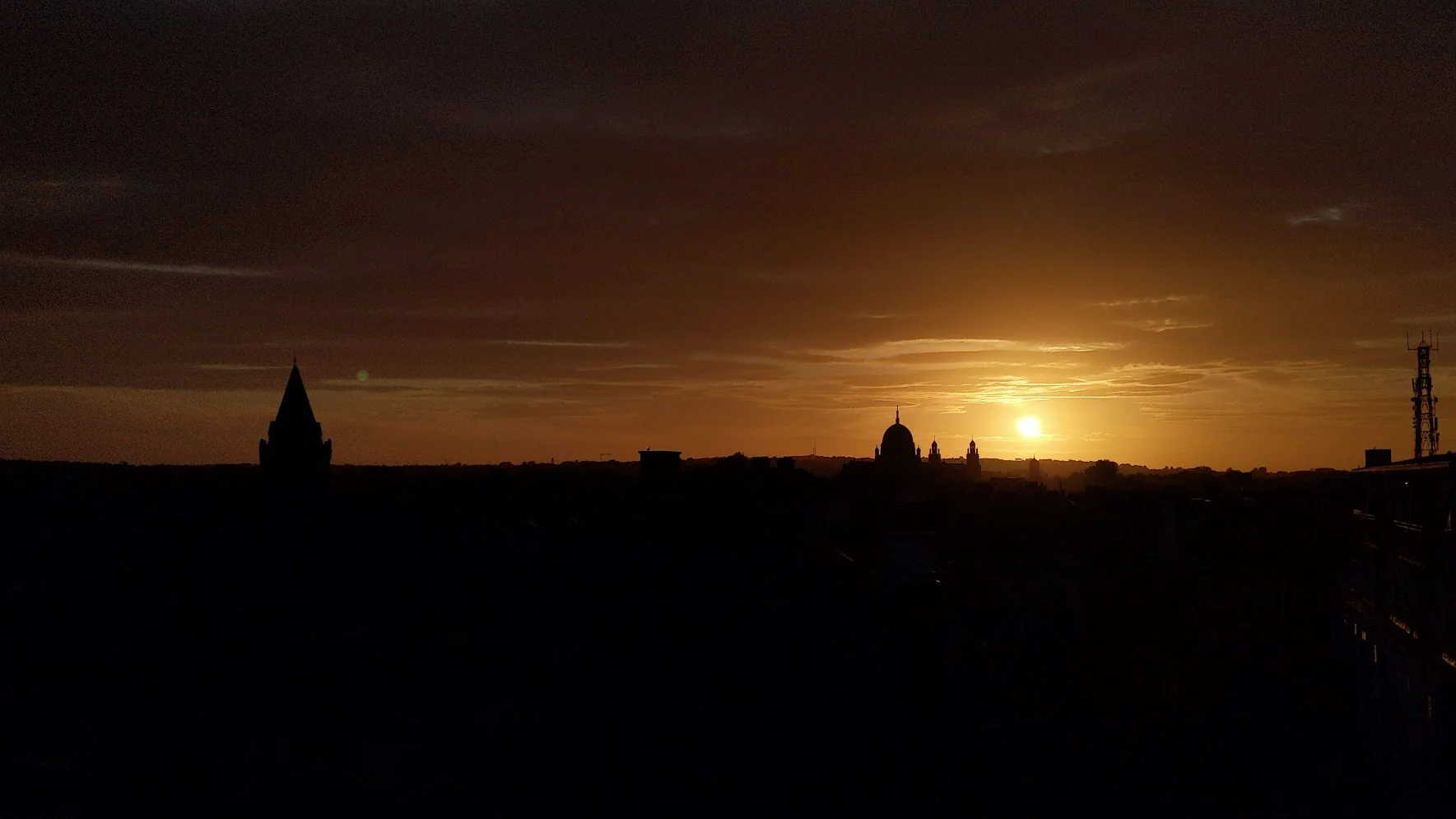 A deep orange sunset silhouettes the towers and domes of Galway against a dark skyline.